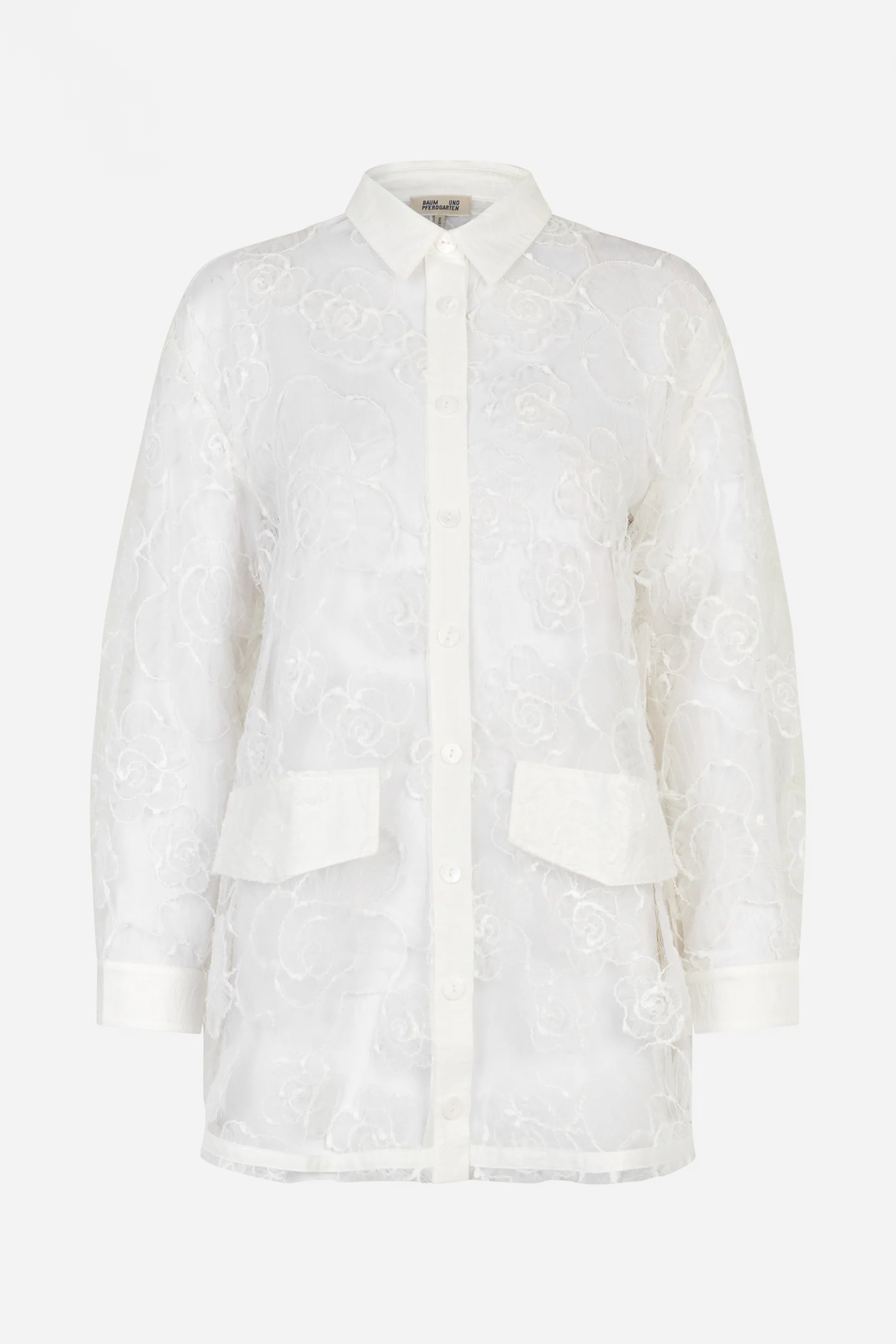 Auf dem Bild ist eine weiße, transparente Spitzenbluse auf weißem Hintergrund zu sehen. Die Bluse hat ein florales Muster, einen klassischen Hemdkragen, eine durchgehende Knopfleiste und zwei aufgesetzte Taschen mit Klappen auf der Vorderseite. Die Ärmel sind lang und enden in weißen Manschetten.
