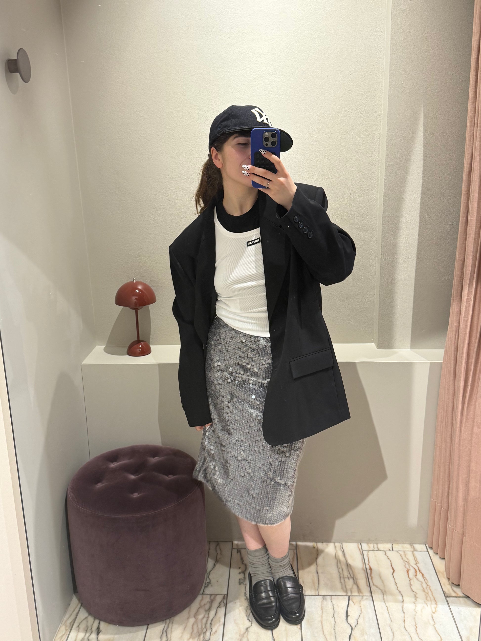 Frau macht Selfie im Spiegel, sie trägt einen silbernen Paillettenrock mit Oversized Blazer und weißen Top. Der Rock ist wadenlang und schimmert im Licht.