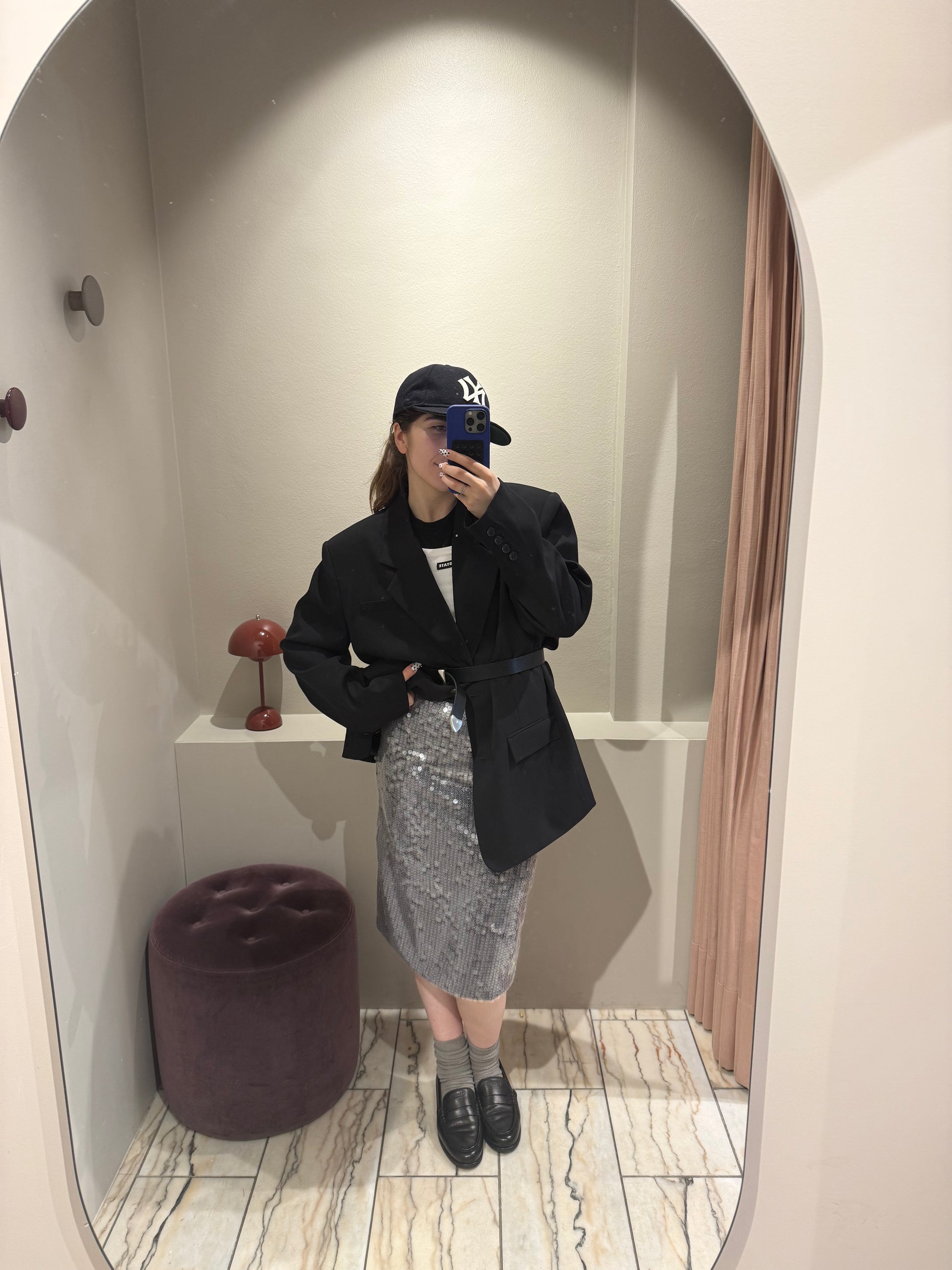 Frau macht Selfie, sie trägt einen silbernen Paillettenrock mit Oversized Blazer und weißen Top. Der Rock ist wadenlang und schimmert im Licht.