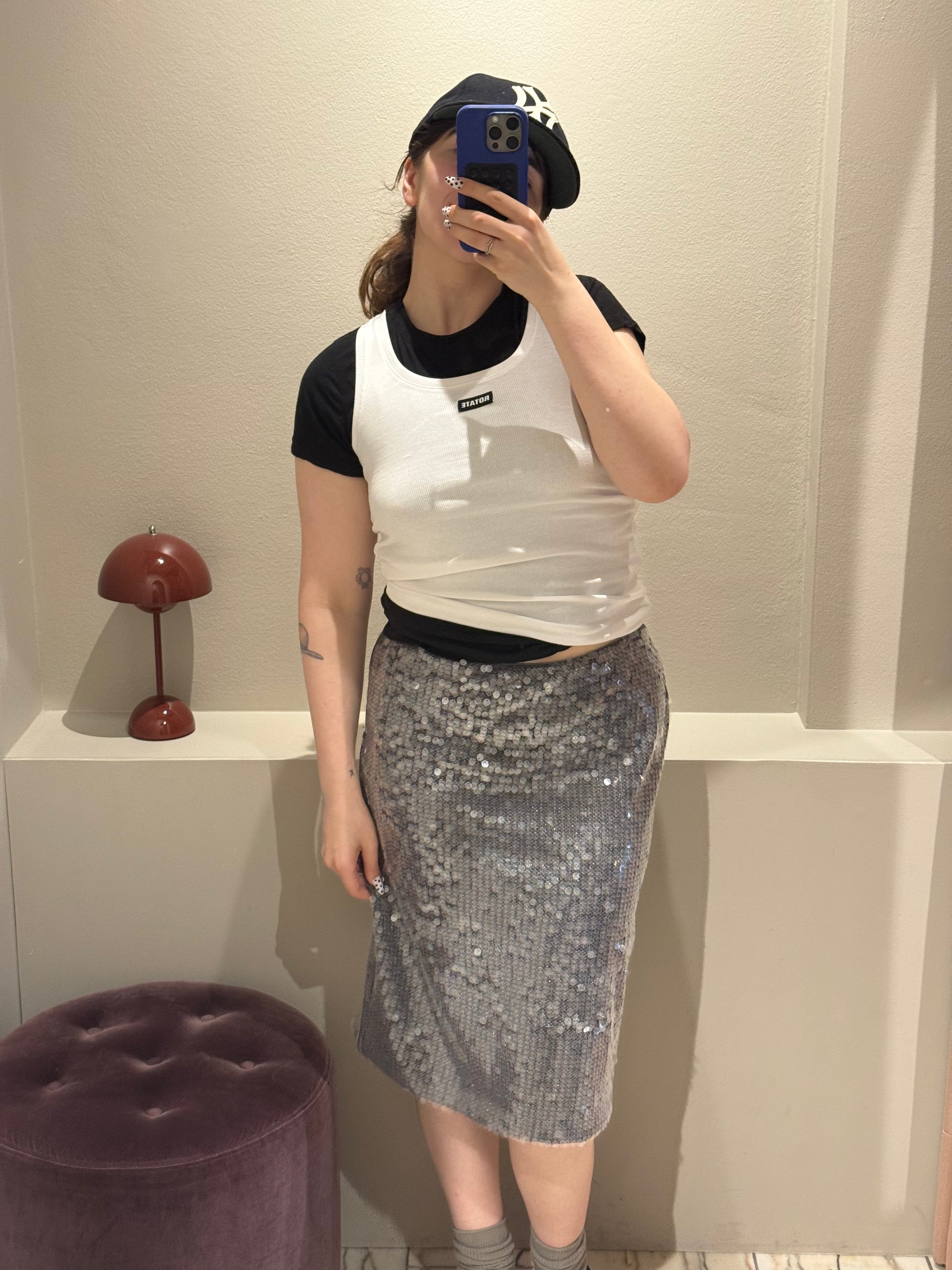 Frau macht Selfie, sie trägt einen silbernen Paillettenrock mit  schwarzem Tshirt und darüber ein weißes Top. Der Rock ist wadenlang und schimmert im Licht.