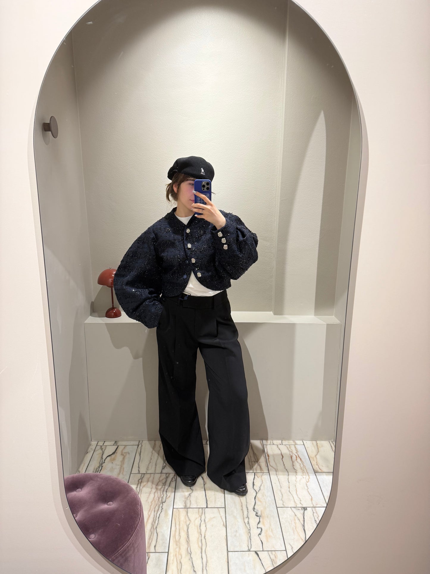 Frau mit schwarzer Bundfaltenhose, dazu Loafer und eine dunkleblaue Bouclejacke die mit schwarzen Paillieten besetzt ist.
