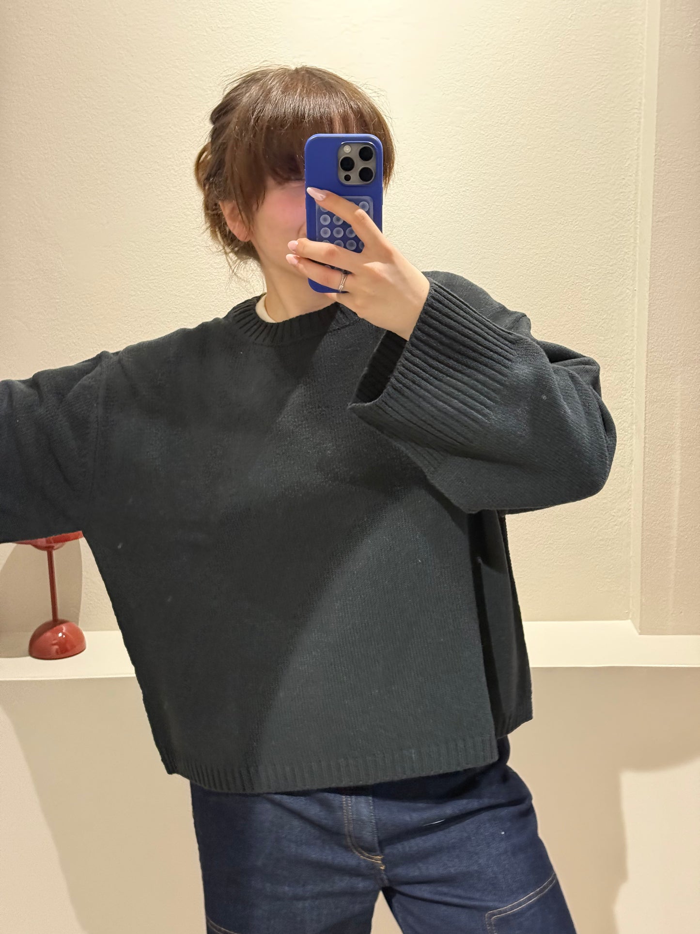 Frau macht Spiegelselfie, sie trägt eine dunkle Jeans und einen waldgrünen Strick mit kastigem Schnitt.