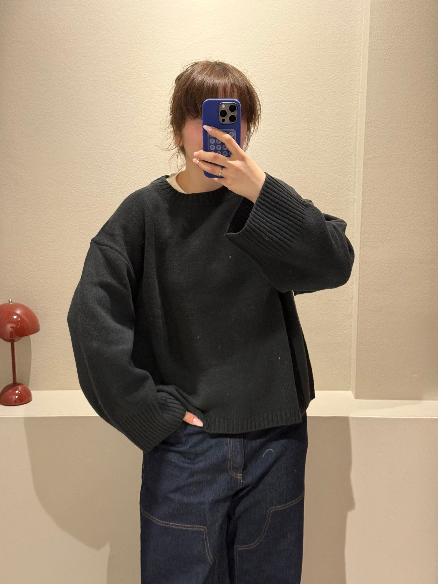 Frau macht Spiegelselfie, sie trägt eine dunkle Jeans und einen waldgrünen Strick mit kastigem Schnitt.