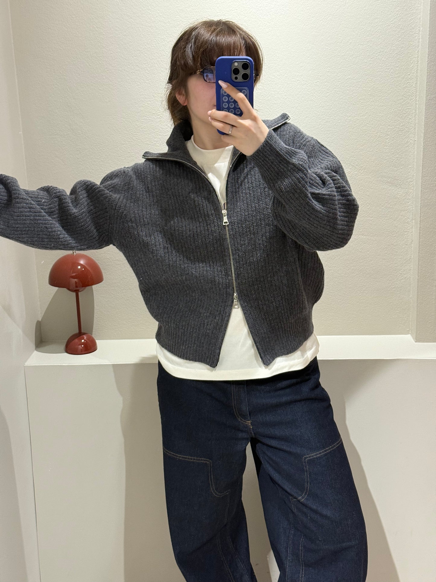 Frau macht Spiegeselfie, sie trägt eine graue Grobstickjacke mit hohem Kragen, dazu eine dunkle Jeans.