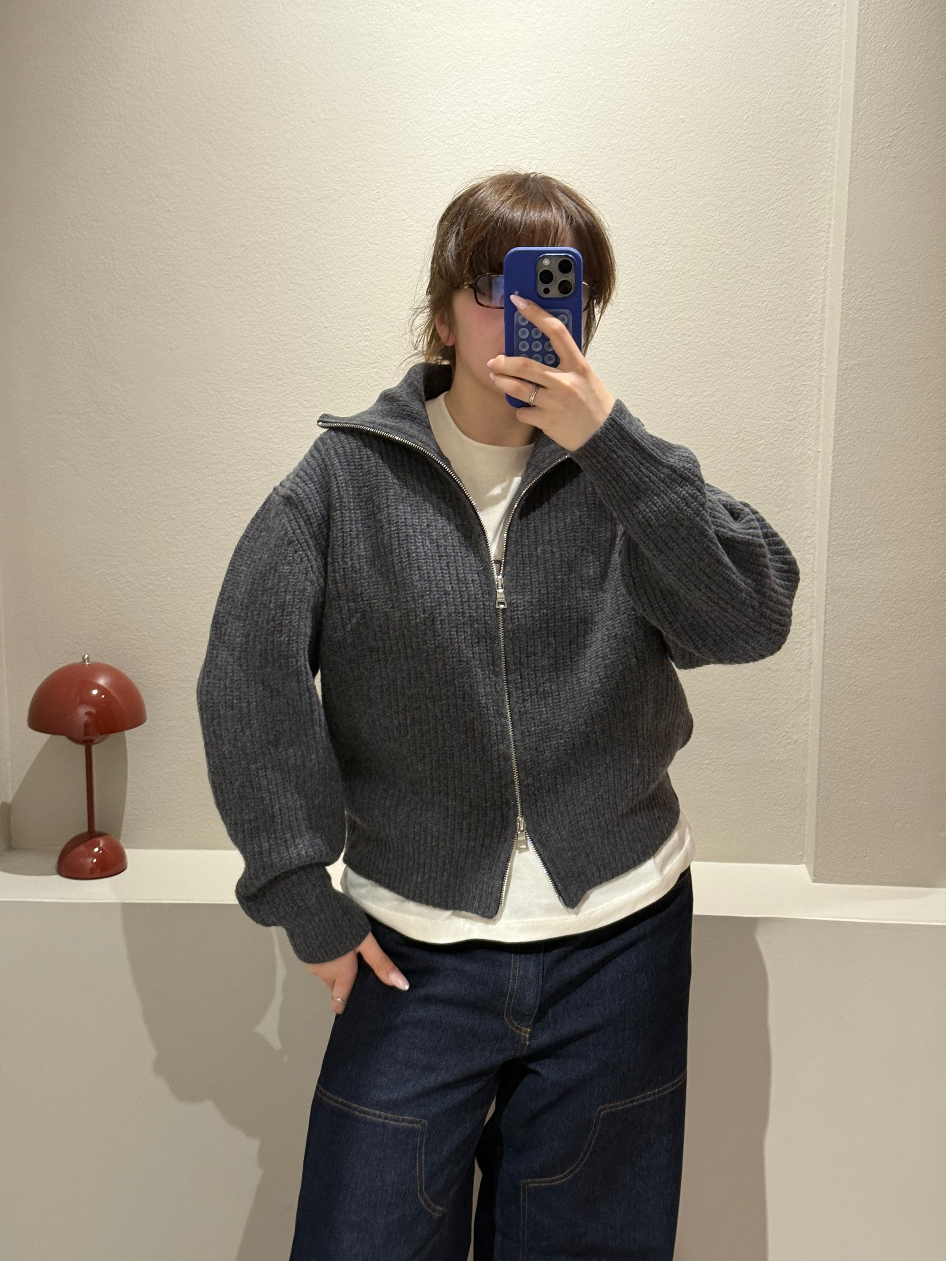 Frau macht Spiegeselfie, sie trägt eine graue Grobstickjacke mit hohem Kragen, dazu eine dunkle Jeans.