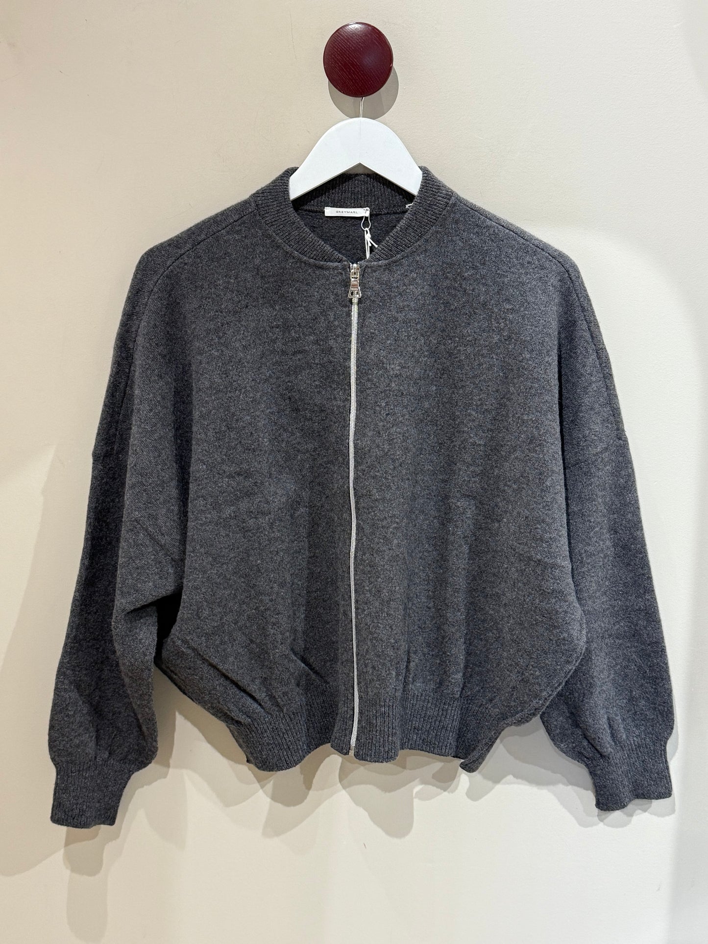 Dunkelgraue Strickbomber vor weißer Wand.