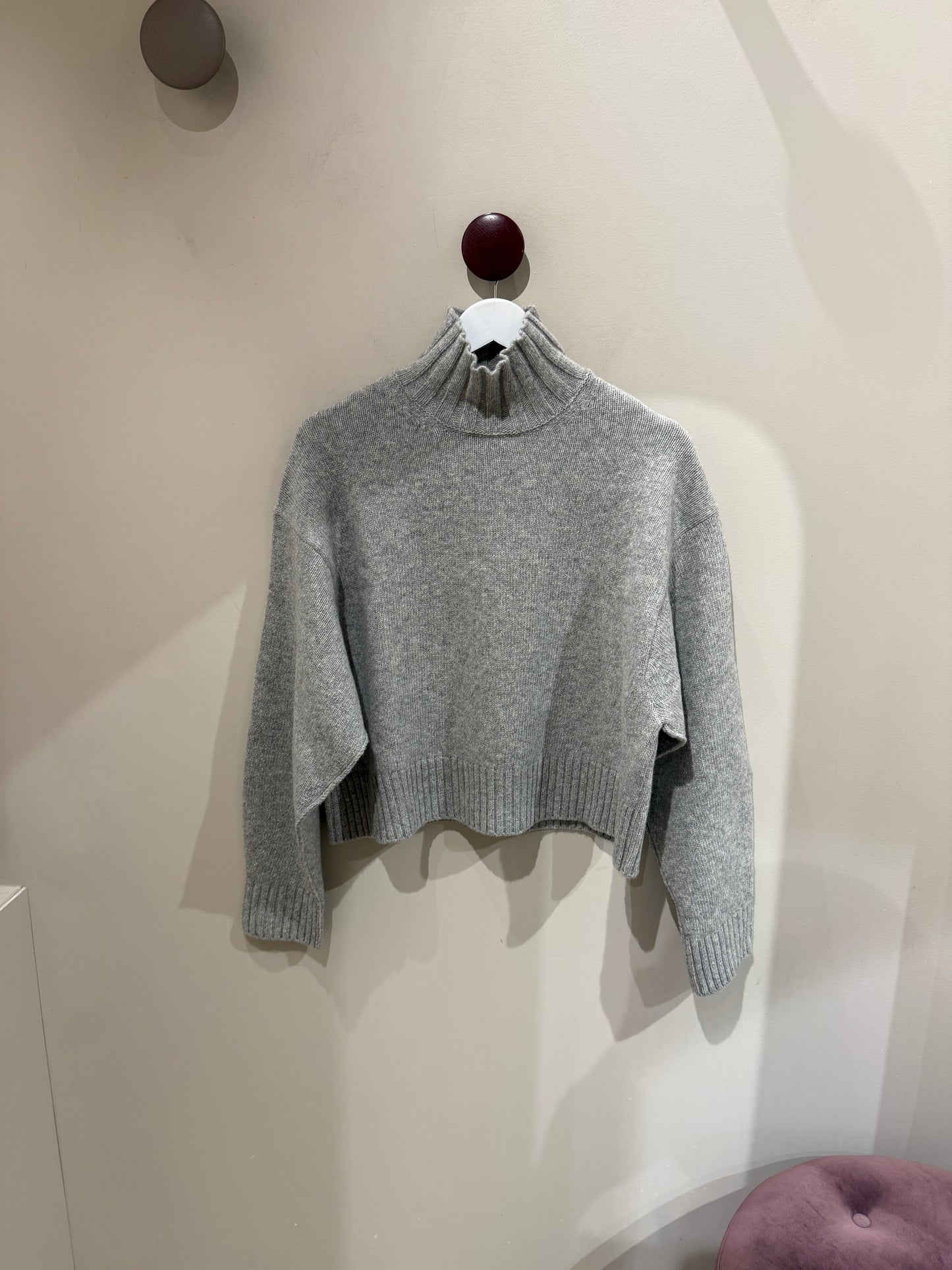Grauer Turtleneck vor weißer Wand.