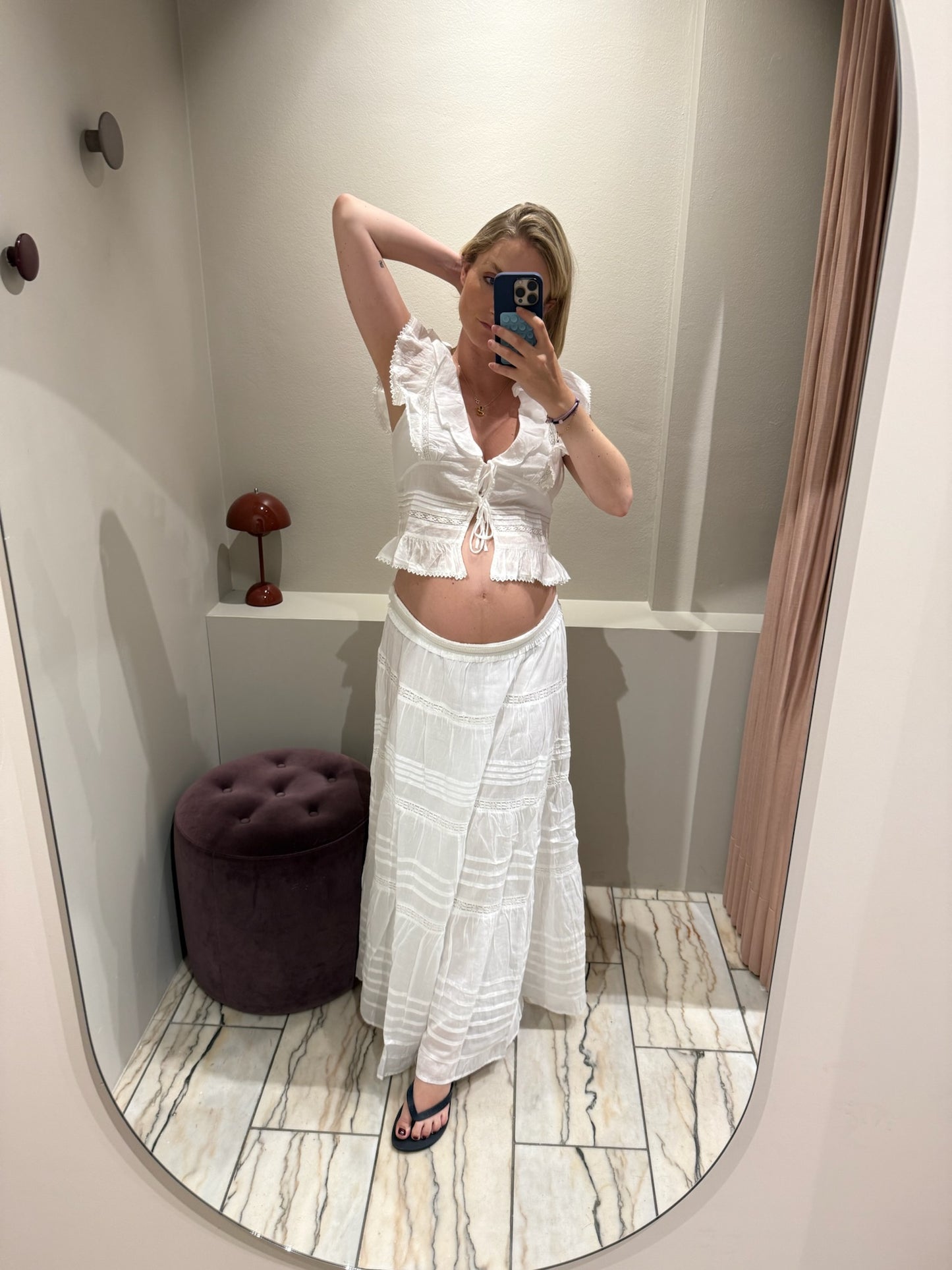 Eine Frau macht ein Spiegel Selfie, sie trägt einen weißen Rock mit horizontalen  Lochstick-Streifen und Rüsschensaum, dazu Flip Flops und eine kurärmige Voilantbluse.