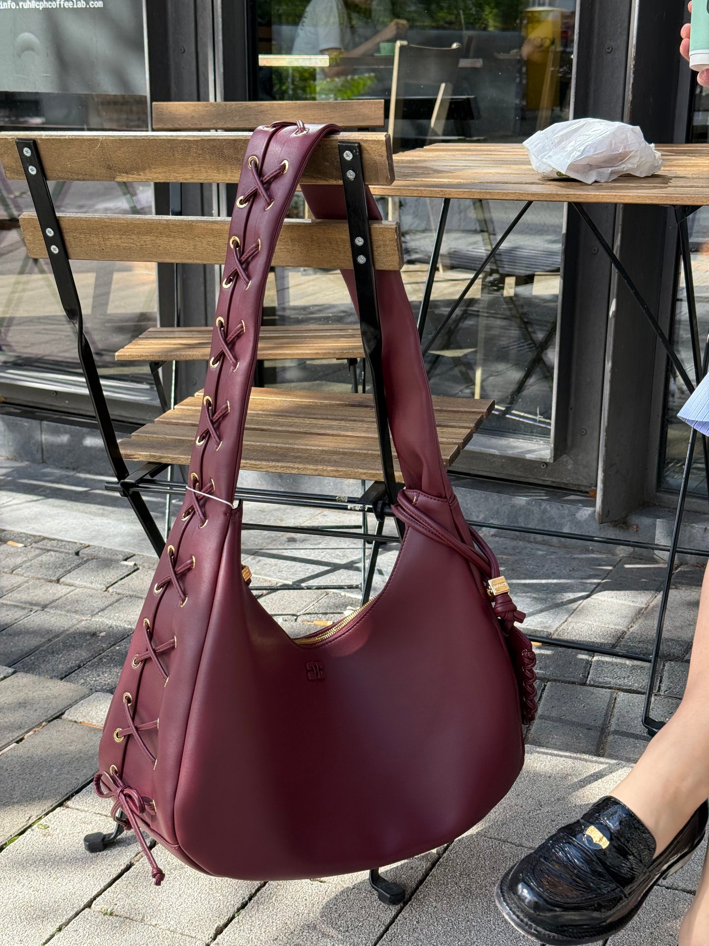 Weinrote Tasche hängt an einem Stuhl, sie hat Schnürrdetails und goldenen Hardware.