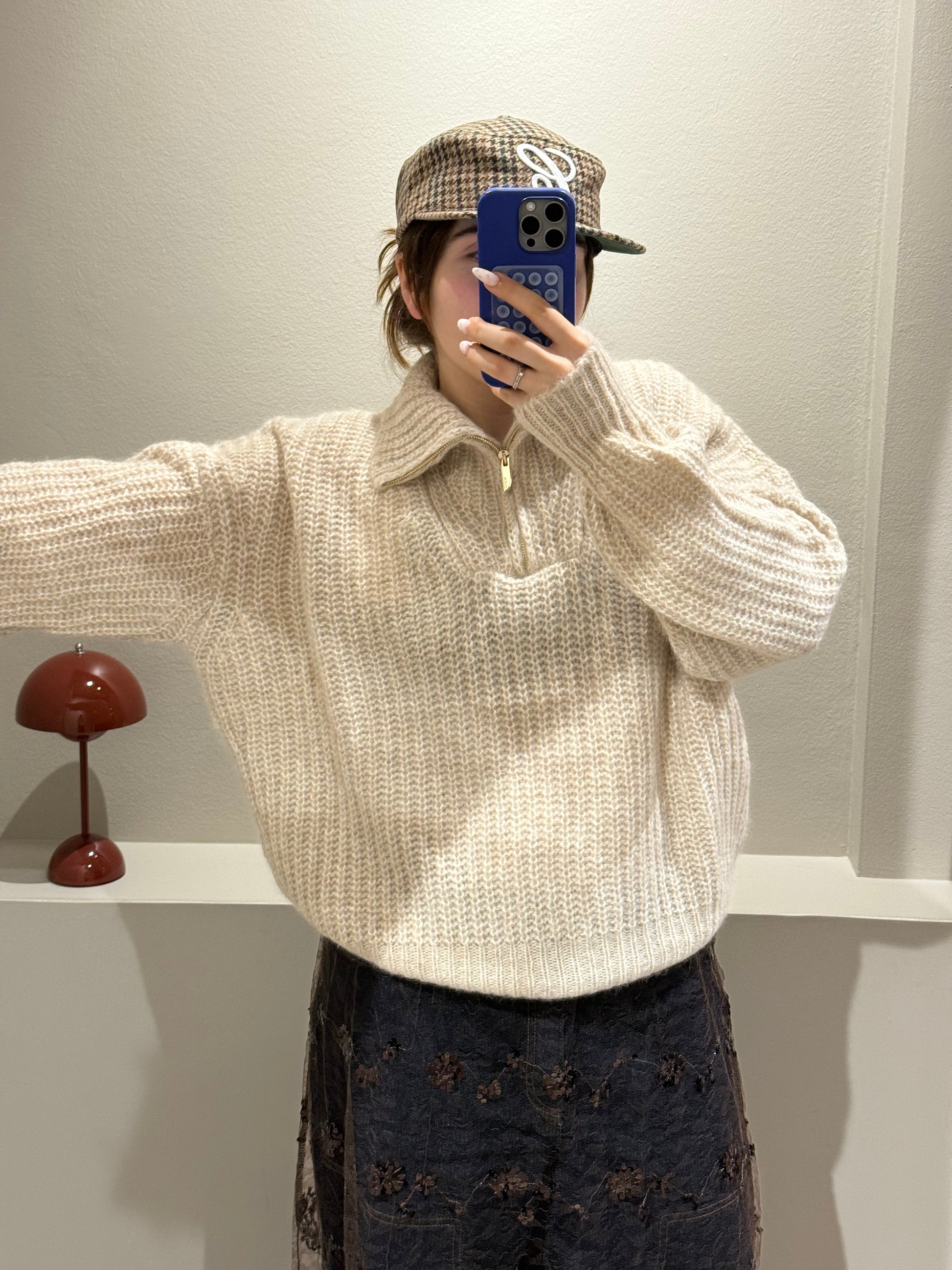 Frau macht Spiegelselfie sie trägt einen beigen Strick und dazu Jeans mit Spitzenrock darüber. Der Strick ist kastig geschnitten und hat einen Quarterzip.