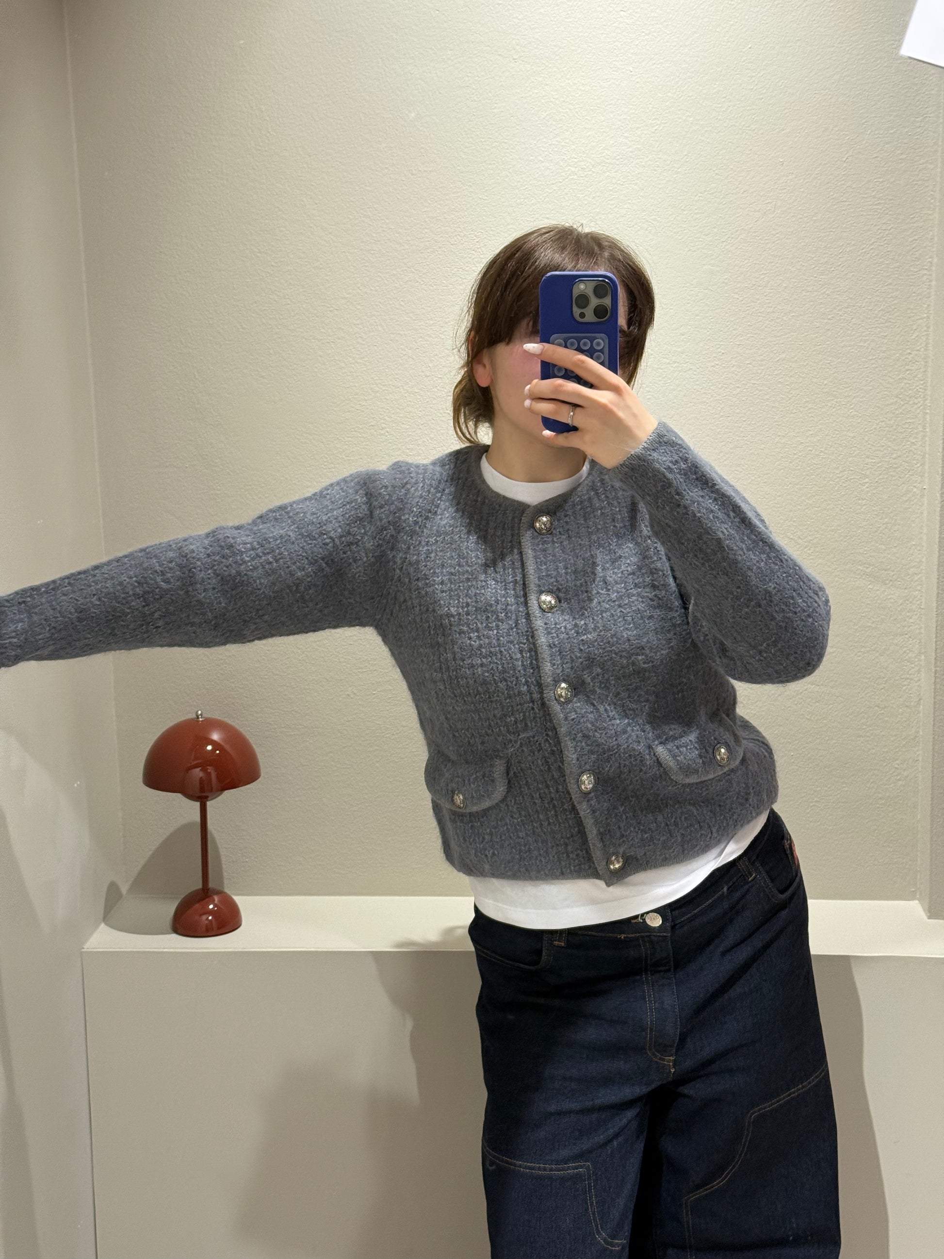 Frau macht Spiegelselfie sie trägt eine dunkle Jeans und grauen Cardigan mit Knöpfen.