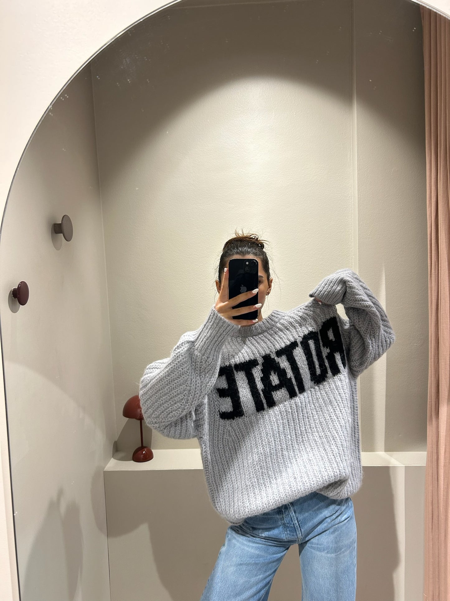 Frau macht Spiegelselfie, sie trägt Jeans und einen grauen kastigen Strickt mit Rotate Schriftzug.