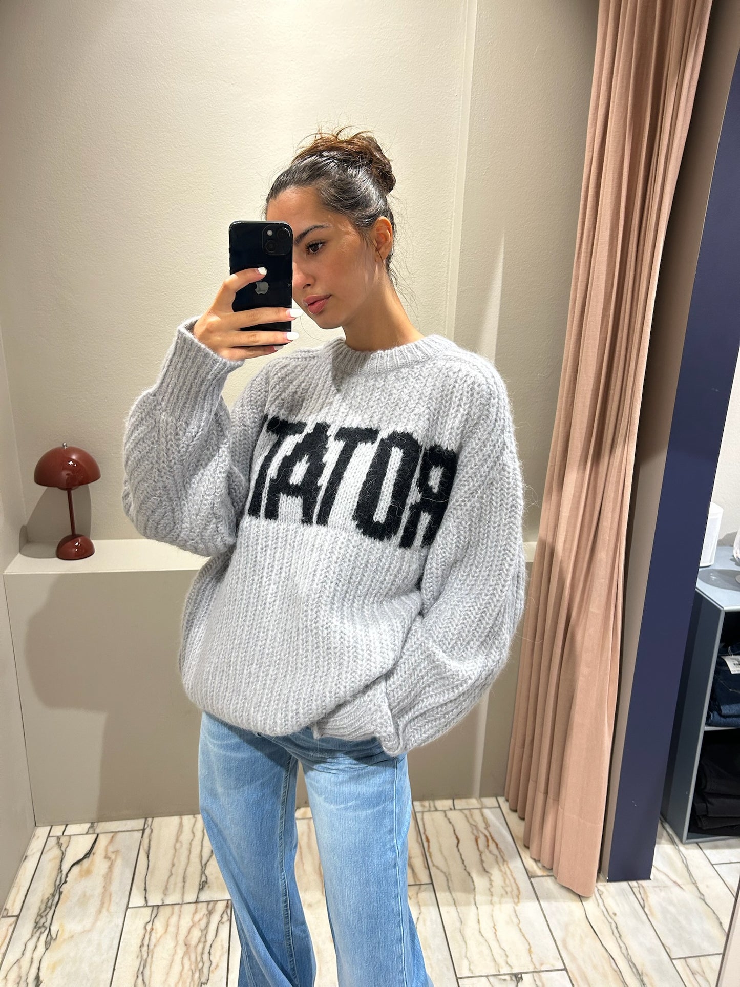 Frau macht Spiegelselfie, sie trägt Jeans und einen grauen kastigen Strickt mit Rotate Schriftzug.