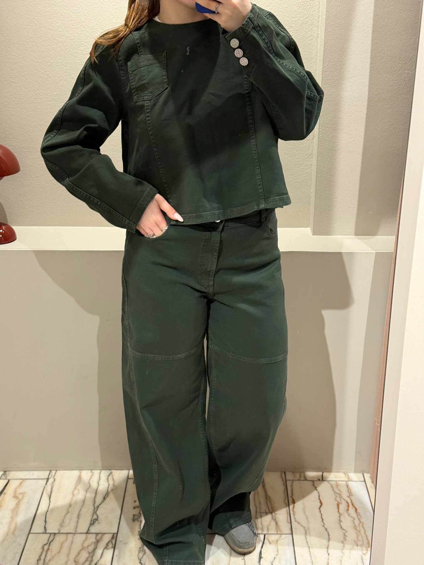 Frau macht Spiegelselfie in grünem Jenas Outfit bestehend aus Bluse und weiter Jeans.