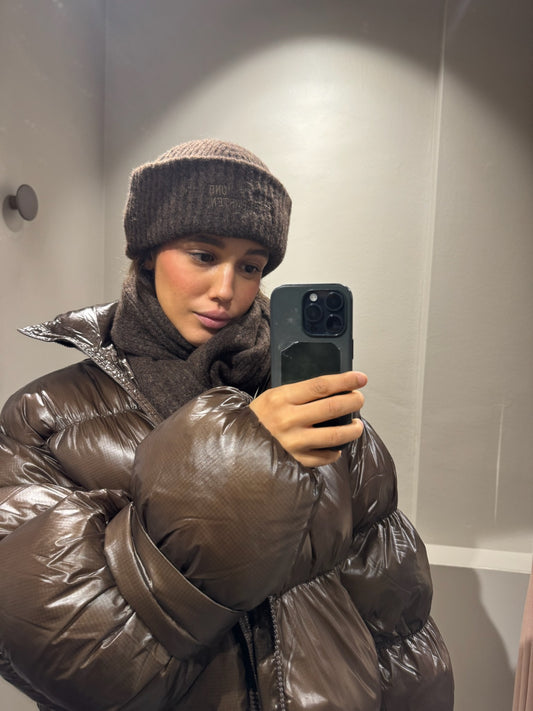 Frau macht Spiegelselfie, sie trägt braune Puffer und dazu passend chal und Mütze.