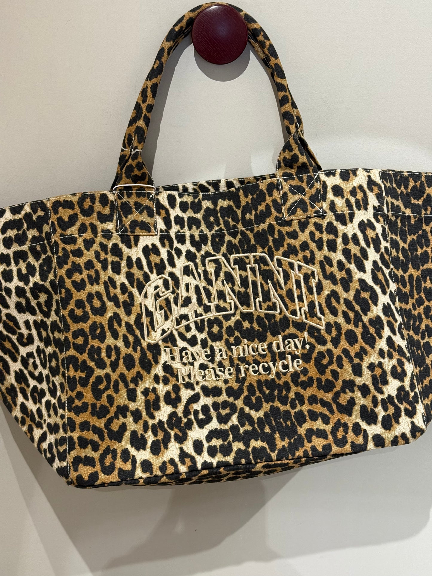 XXL-Shopper von Ganni aus recyceltem Baumwoll-Canvas mit Leopardenmuster, aufgesticktem „Have a nice day! Please recycle“-Schriftzug, zwei stabilen Tragegriffen und offenem Innenfach. Große, lässige Form.