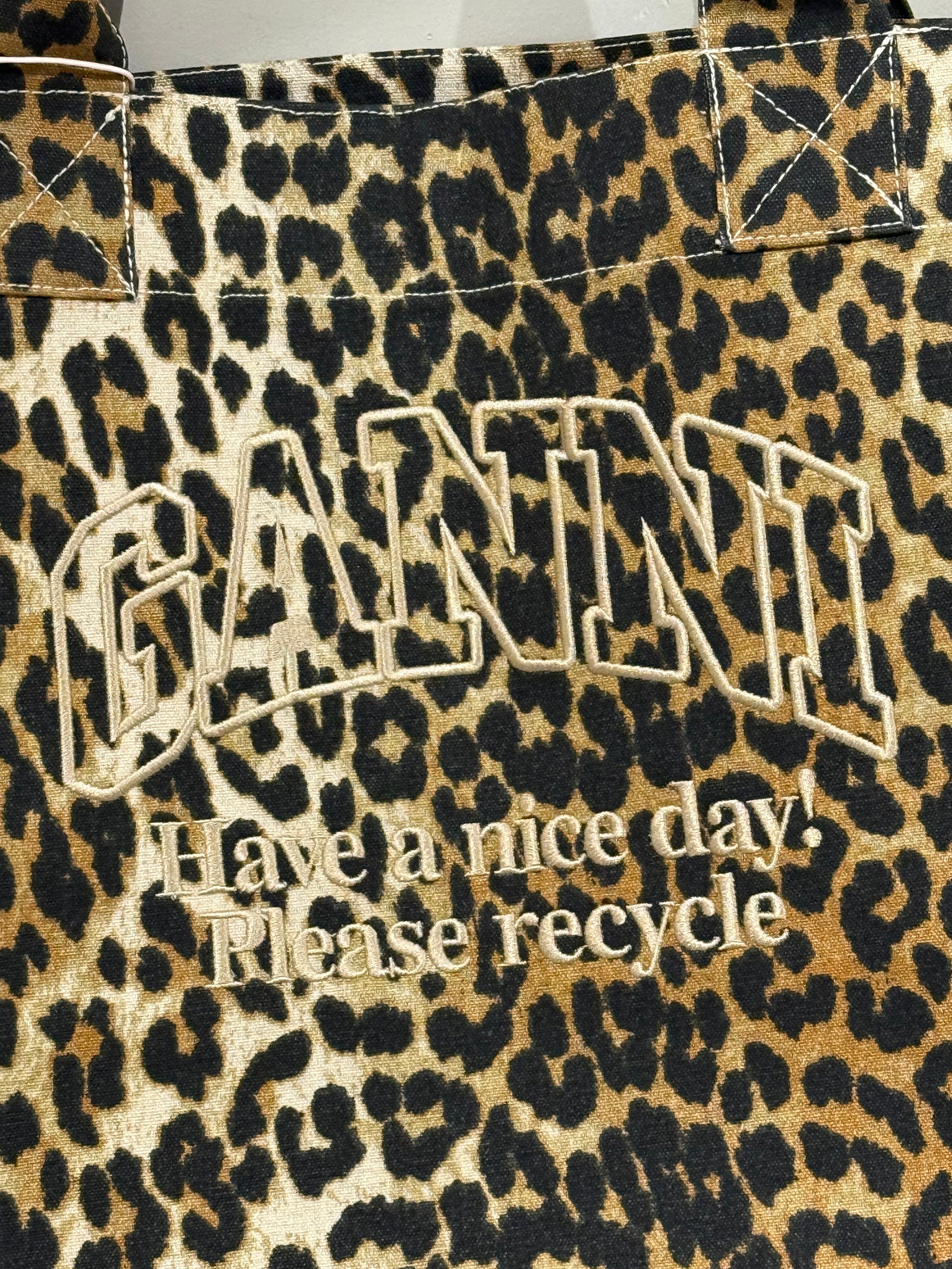XXL-Shopper von Ganni aus recyceltem Baumwoll-Canvas mit Leopardenmuster, aufgesticktem „Have a nice day! Please recycle“-Schriftzug, zwei stabilen Tragegriffen und offenem Innenfach. Große, lässige Form.