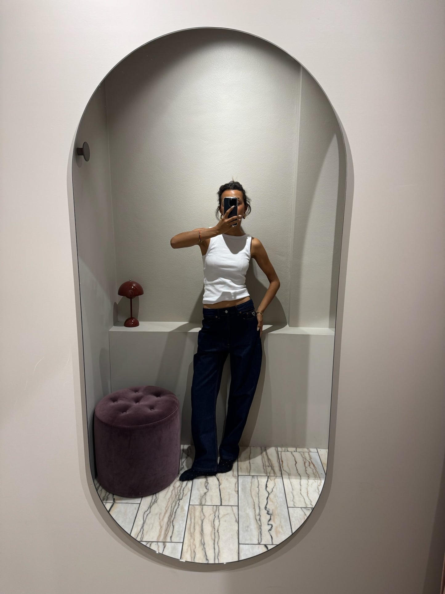 Frau im Spiegel, sie trägt eine dunkleblaue lässige Jeans und ein weißes Top.