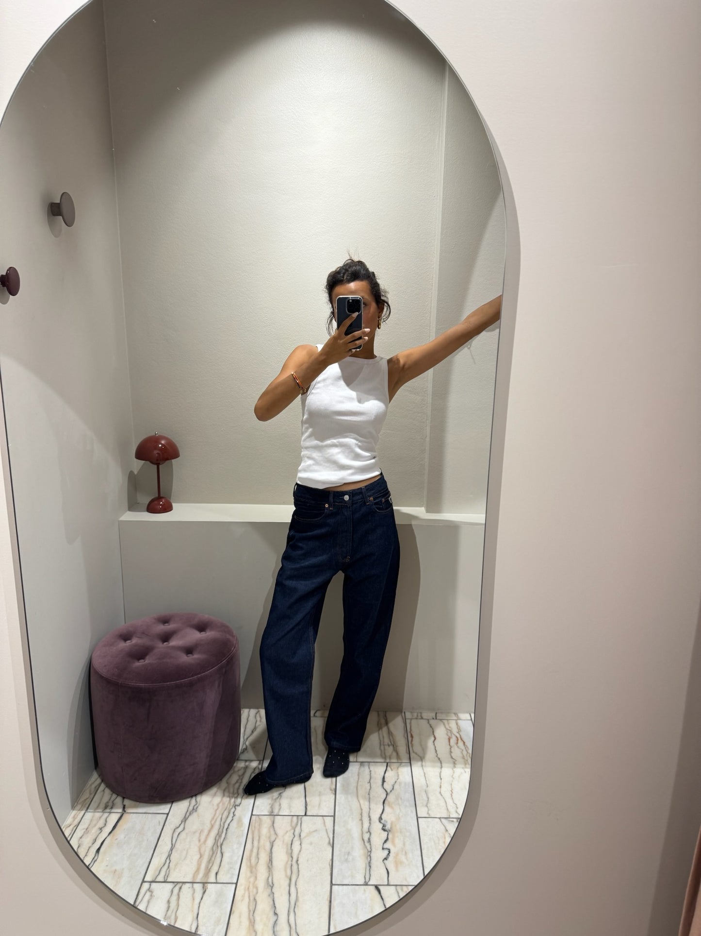 Frau im Spiegel, sie trägt eine dunkleblaue lässige Jeans und ein weißes Top.