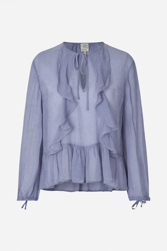 Auf dem Bild ist eine hellfliederfarbene Bluse zu sehen, die auf einem weißen Hintergrund liegt. Die Bluse hat große Volants auf der Vorderseite, einen runden Ausschnitt mit Bindeband und lange Ärmel mit Schleifen an den Bündchen.
