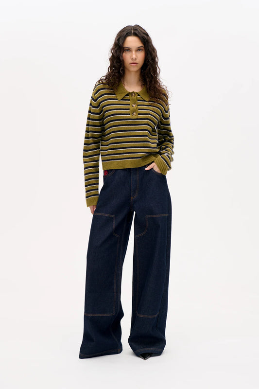 FFrau vor weißer Wand, sie trägt ein grün-gestreiftes Strickpolo und eine weite dark wash Jeans mit Carpenter Detail.