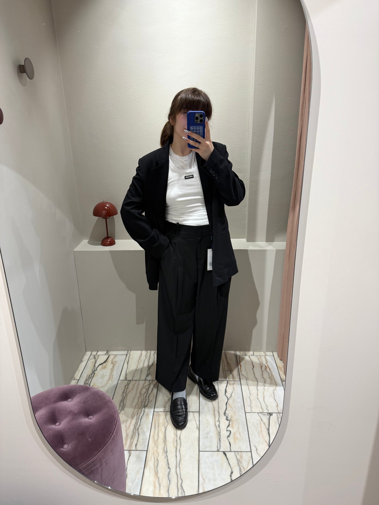 Frau macht Spiegelselfie, sie trägt eine verkürzte Schwarze Bundfaltenhose mit weitem Schnitt und dazu passend einen schwarzen Blazer mit geradem Schnitt.