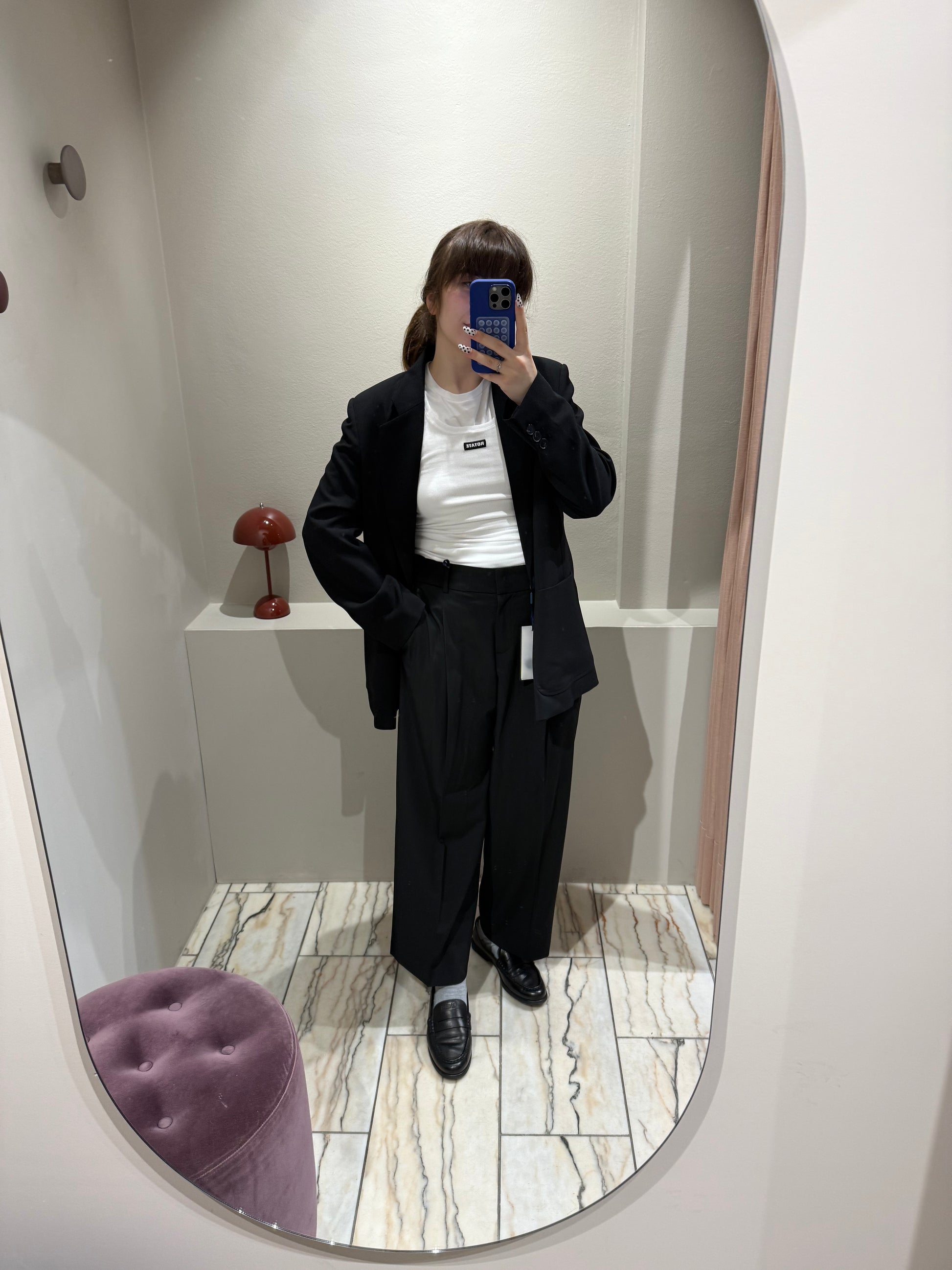 Frau macht Spiegelselfie, sie trägt eine verkürzte Schwarze Bundfaltenhose mit weitem Schnitt und dazu passend einen schwarzen Blazer mit geradem Schnitt.