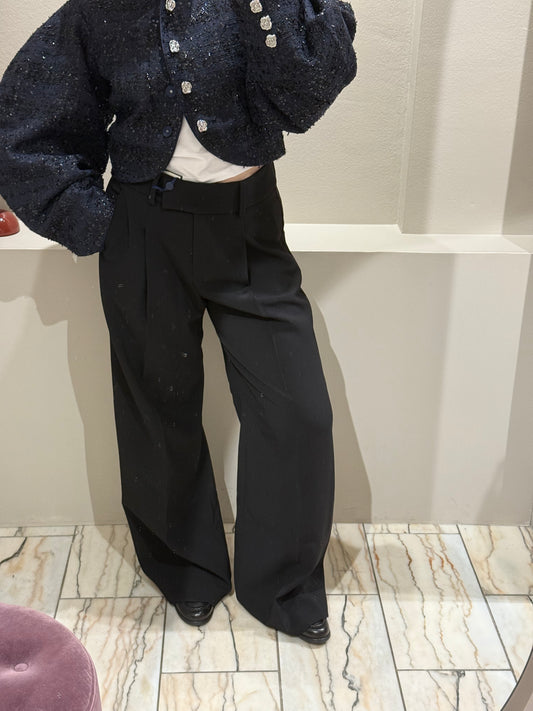 Frau mit schwarzer Bundfaltenhose, dazu Loafer und eine dunkleblaue Bouclejacke die mit schwarzen Paillieten besetzt ist.