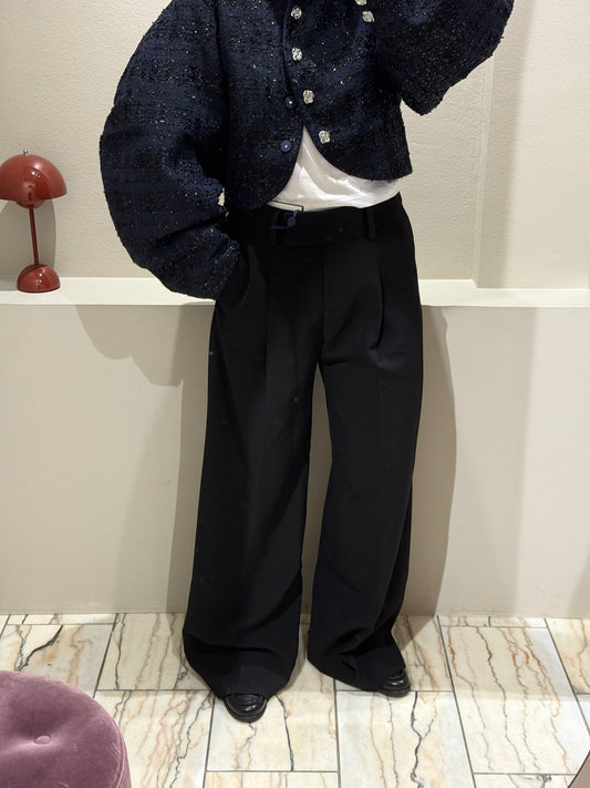 Frau mit schwarzer Bundfaltenhose, dazu Loafer und eine dunkleblaue Bouclejacke die mit schwarzen Paillieten besetzt ist.