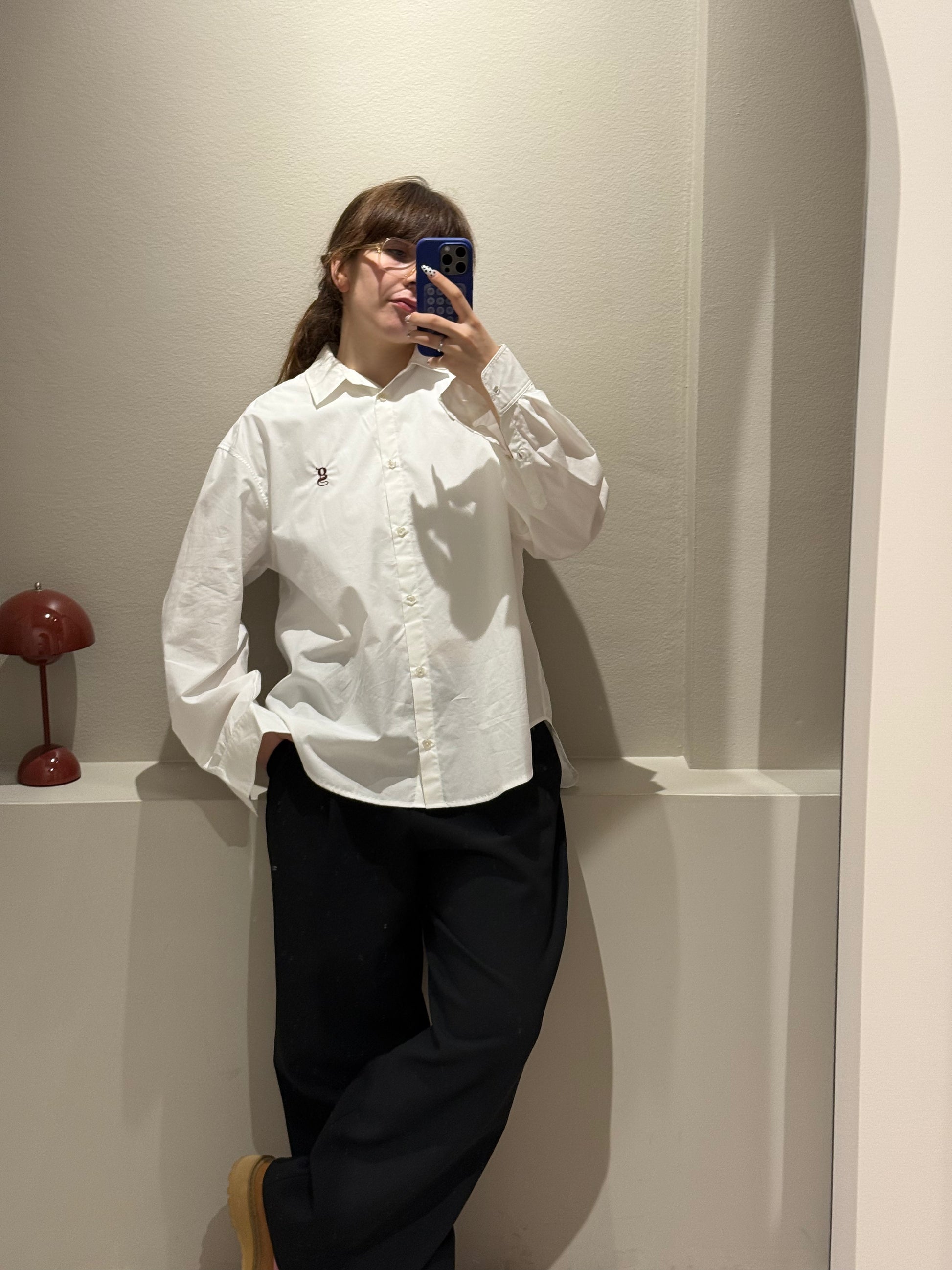 Frau macht Spiegelselfie, im Fokus ist eine weiße Bluse mit aufgesticktem G-Logo.