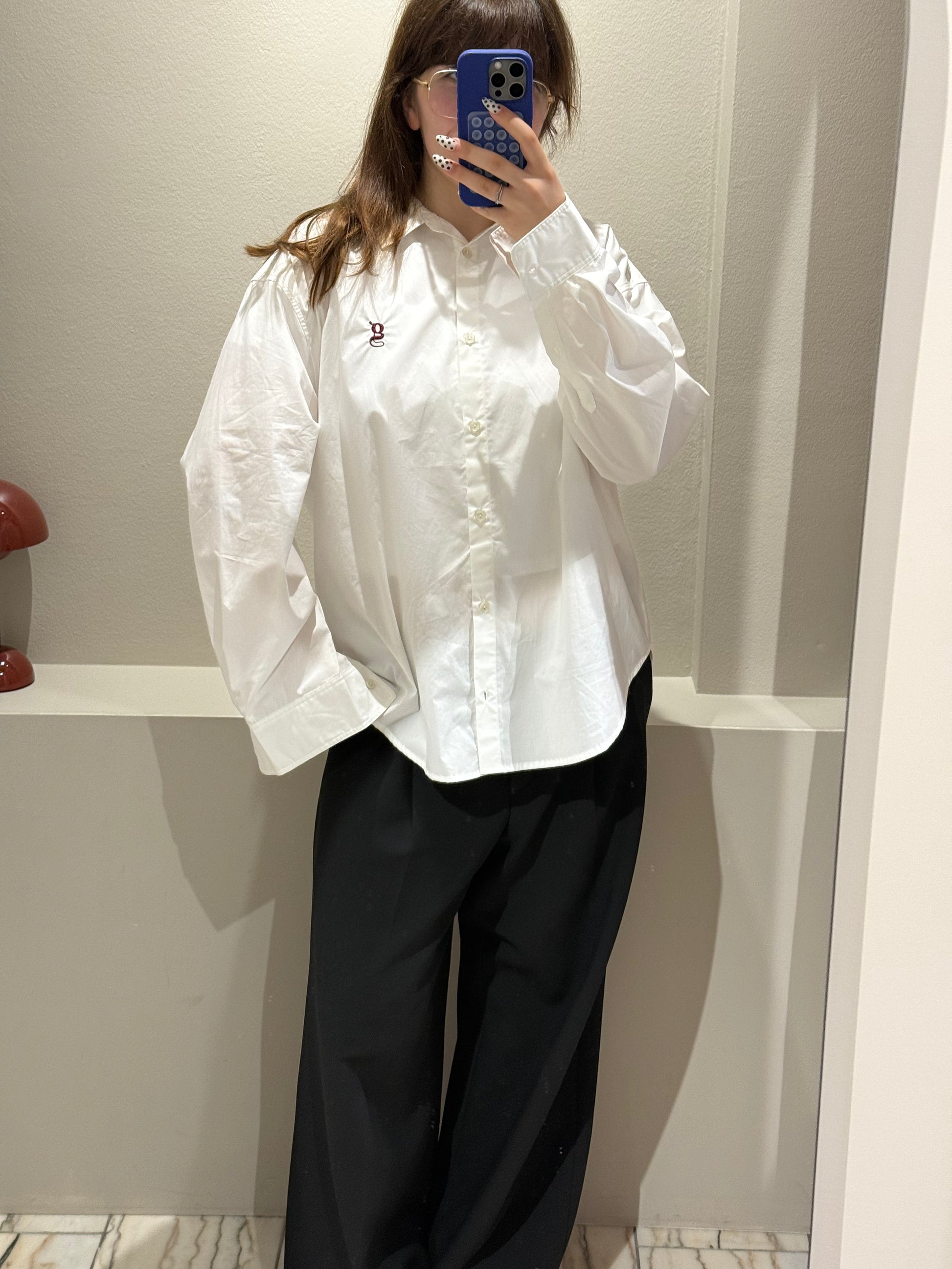 Frau macht Spiegelselfie, im Fokus ist eine weiße Bluse mit aufgesticktem G-Logo.