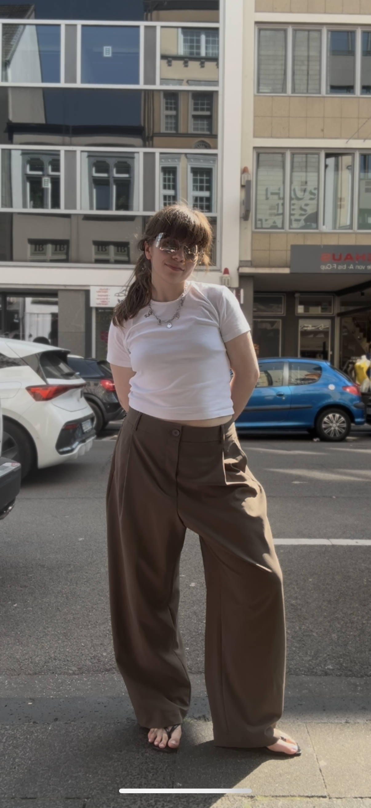 Frau auf der Straße, sie trägt eine Weite Bundfaltenhose mit weißem Tshirt und Flip Flops.