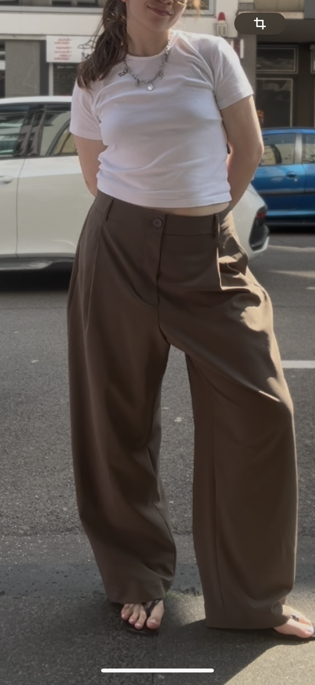 Frau auf der Straße, sie trägt eine Weite Bundfaltenhose mit weißem Tshirt und Flip Flops.