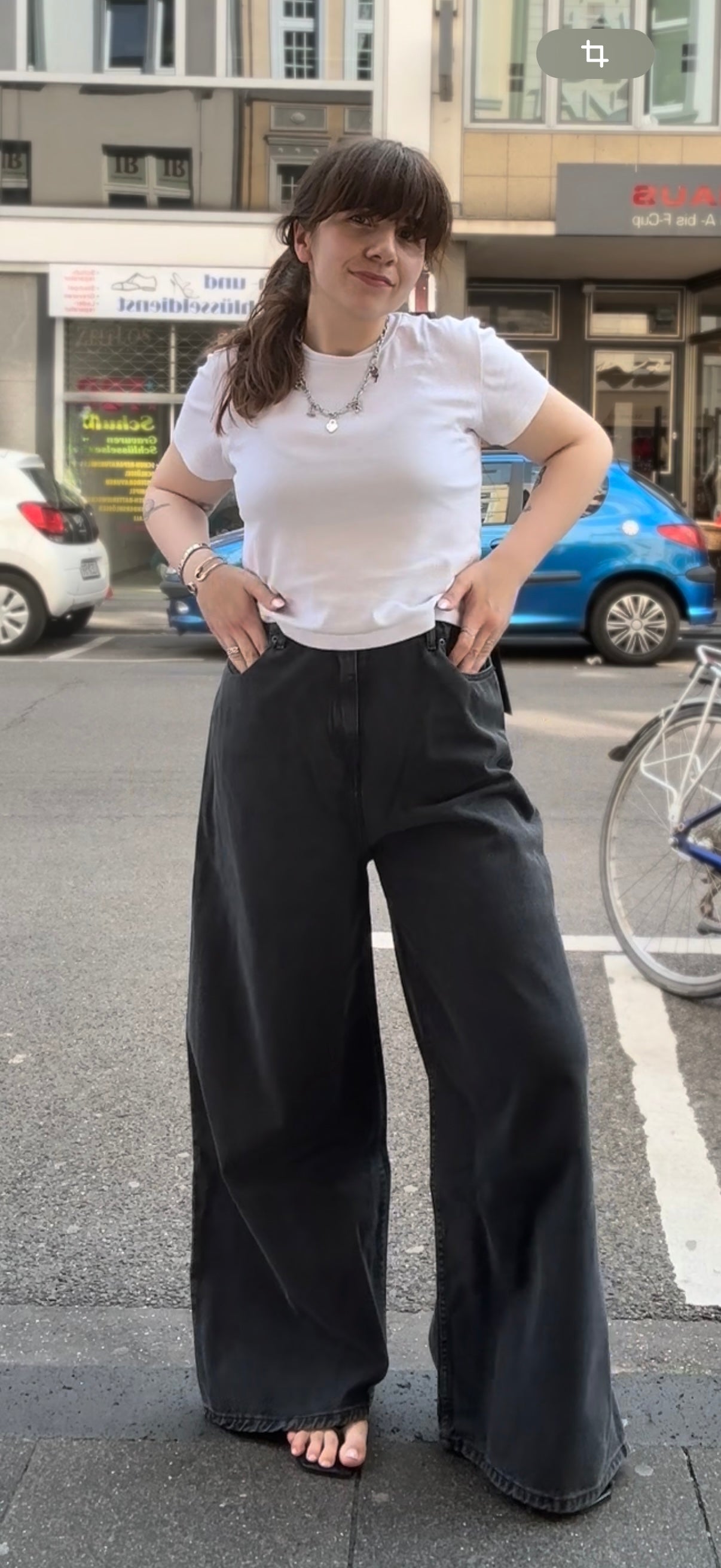 Frau auf der Straße. Sie trägt ein weißes Tshirt mit einer extra weitem Jeans in Grau. dazu Flip FLops und Silberschmuck.