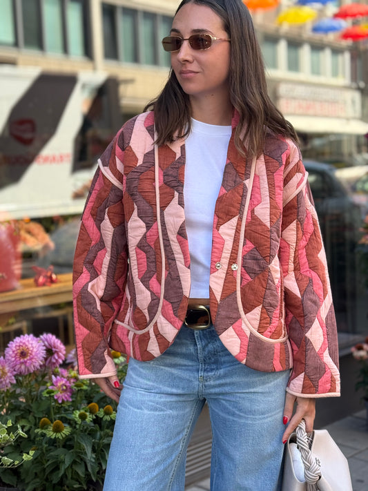 Frau steht vor Blumenladen, sie trägt eine Jacke im Patchwork-Design und dazu eine hellblaue Denim und Sonnebrille.