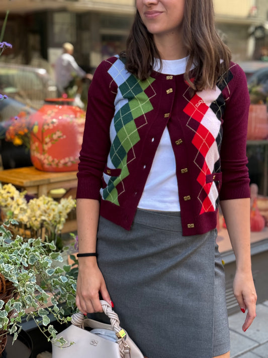 Frau steht vor Blumenladen. Sie trägt einen grauen Minirock, weißes Tshirt und weinroten Cardigan mit buntem Karo.