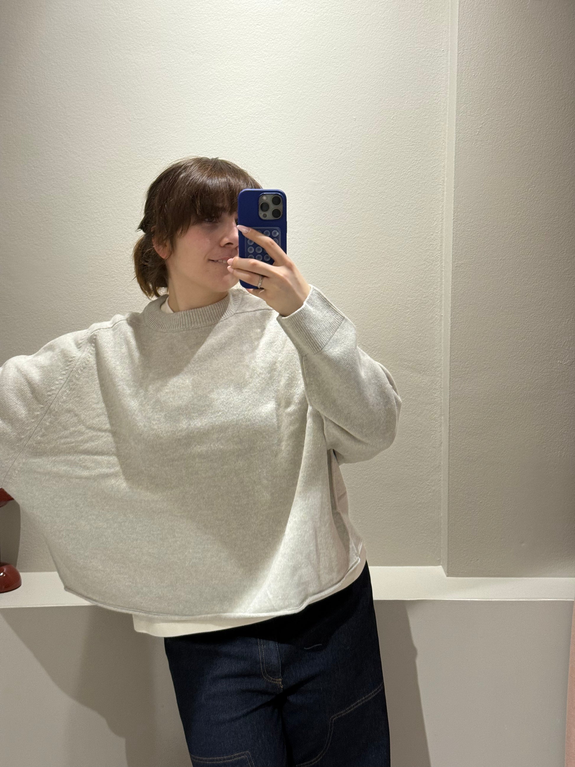 Frau macht spiegelselfie mit hellgrauem oversized Strick.