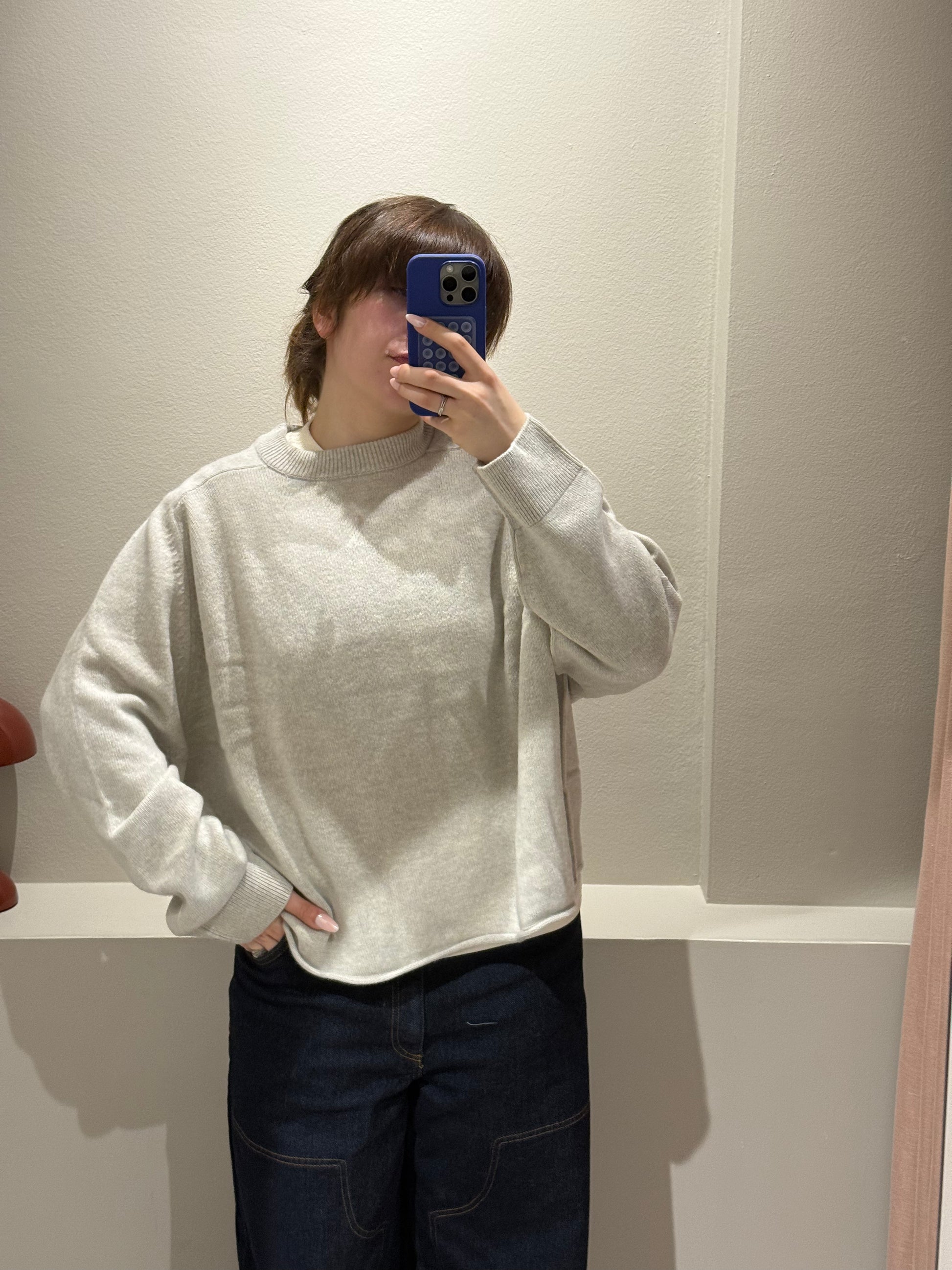 Frau macht Spiegelselfie mit hellgrauem oversized Strick.