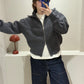 Frau macht Spiegeselfie, sie trägt eine graue Grobstickjacke mit hohem Kragen, dazu eine dunkle Jeans.