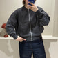 Frau macht Spiegelselfie, sie trägt iene dunkelgraue Strickbomberjacke und dunkle Jeans.