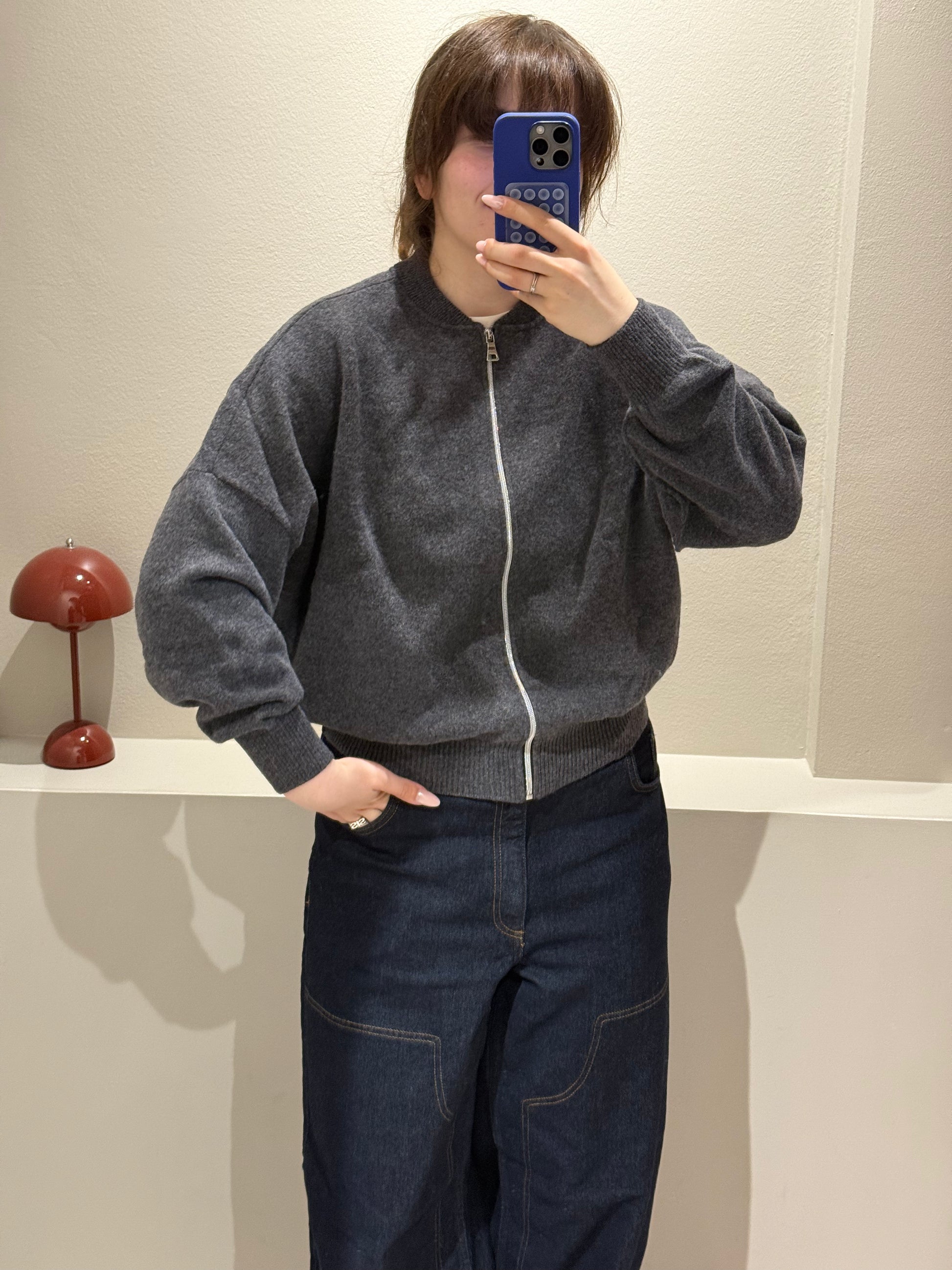 Frau macht Spiegelselfie, sie trägt iene dunkelgraue Strickbomberjacke und dunkle Jeans.