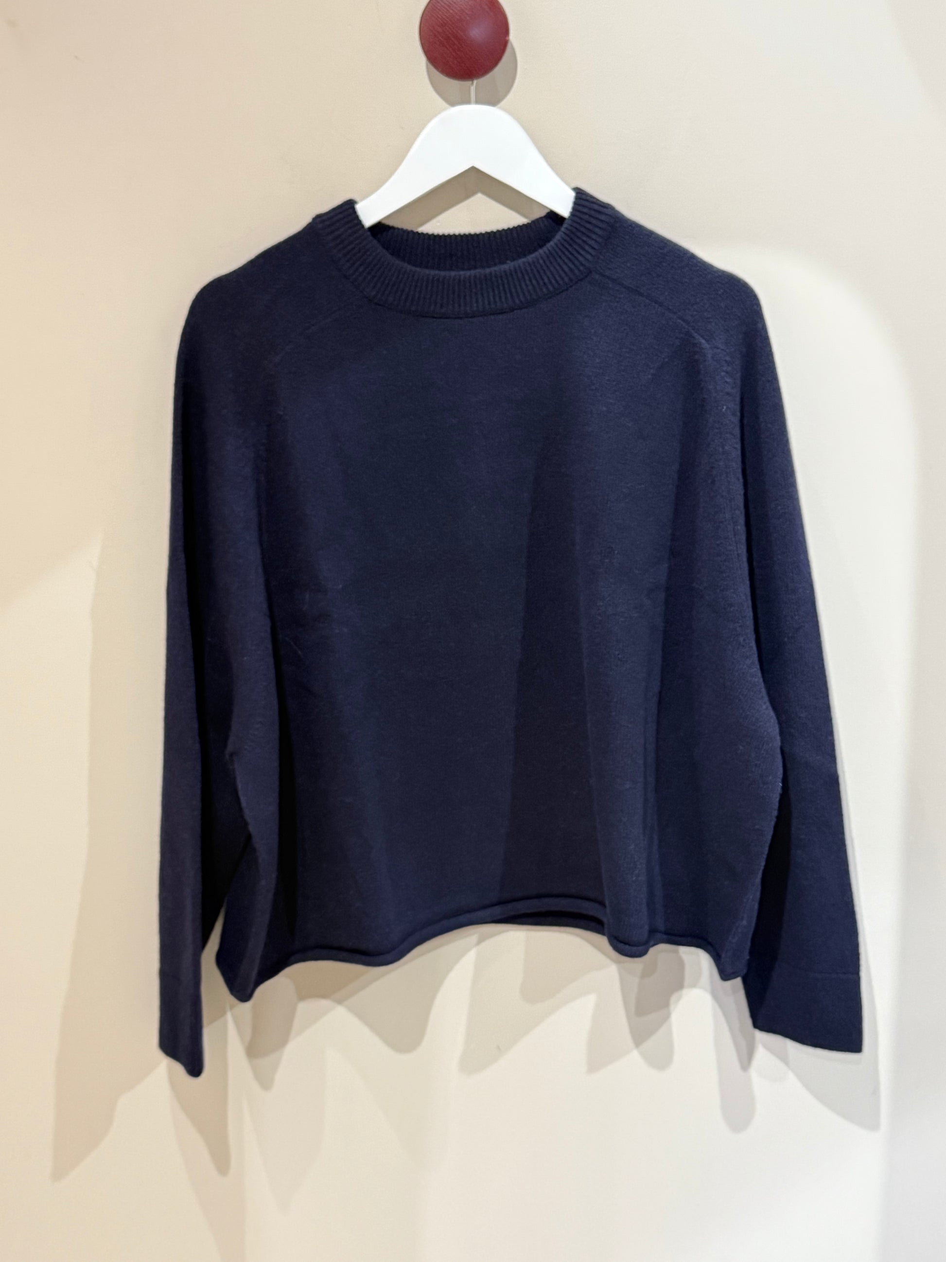 Blauer Strick vor weißer Wand, Crewnack mit rohem Bund unten.
