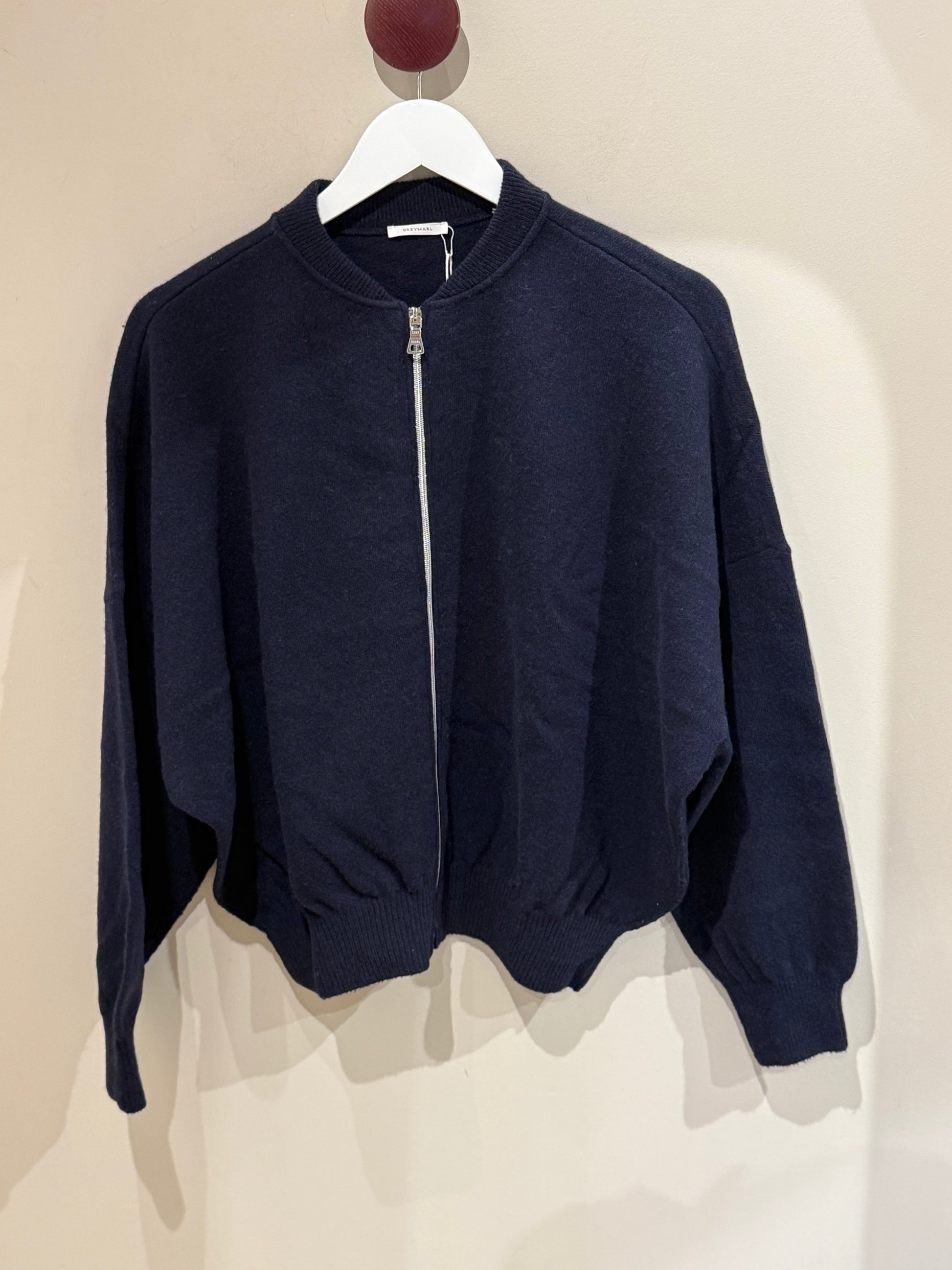 Dunkelblaue Strickbomber vor weißer Wand.