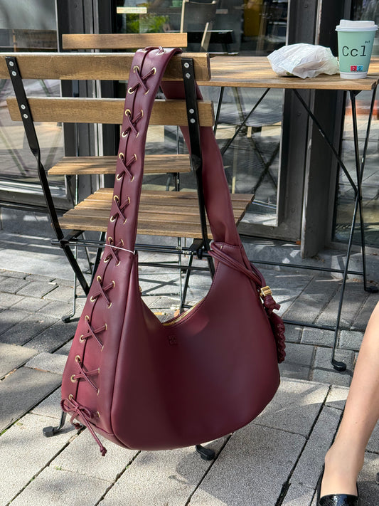 Weinrote Tasche hängt an einem Stuhl, sie hat Schnürrdetails und goldenen Hardware.