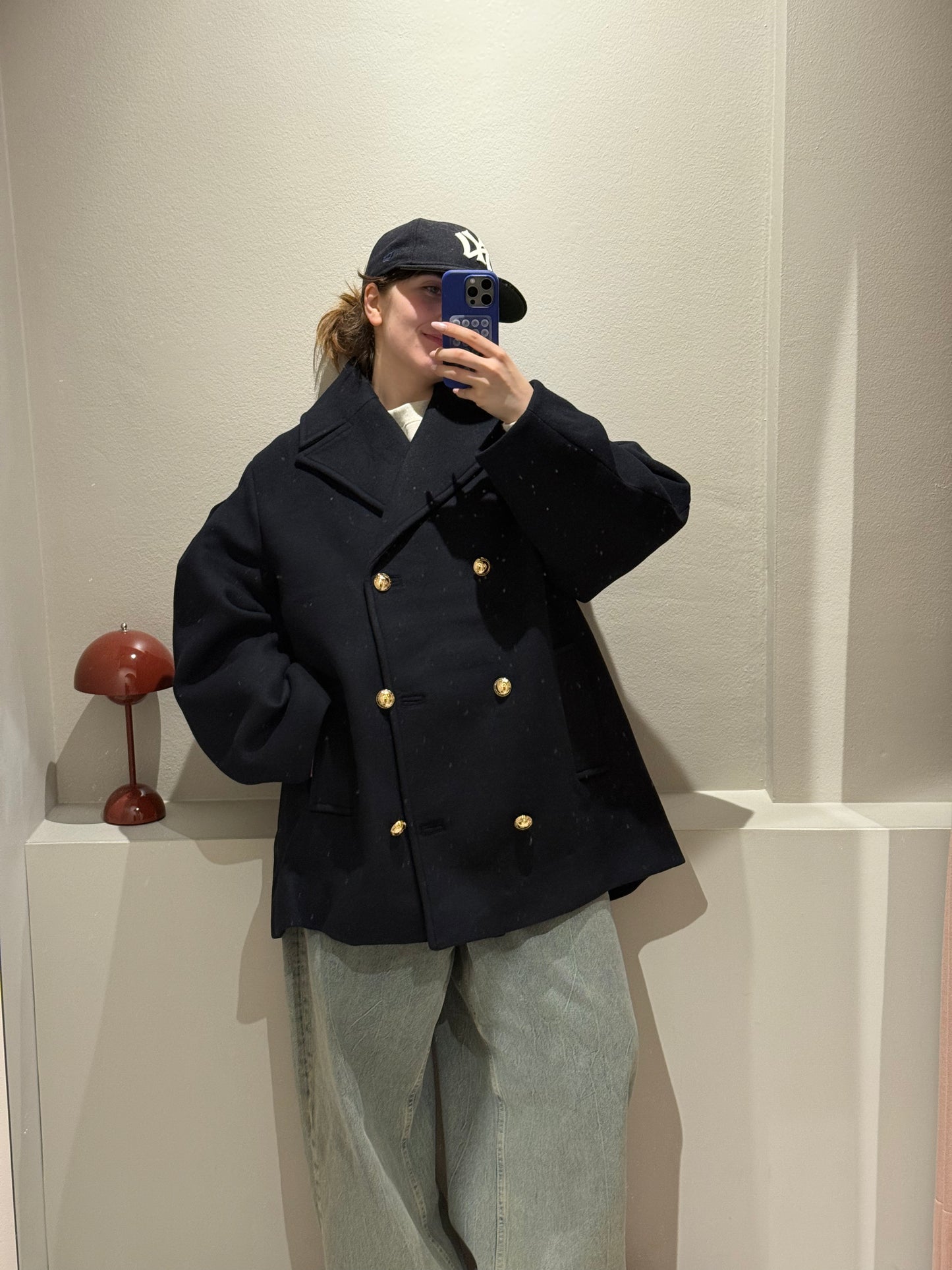 Frau macht Spiegelselfie, sie trägt eine dunkelblaue Cabanjacke und Jeans.