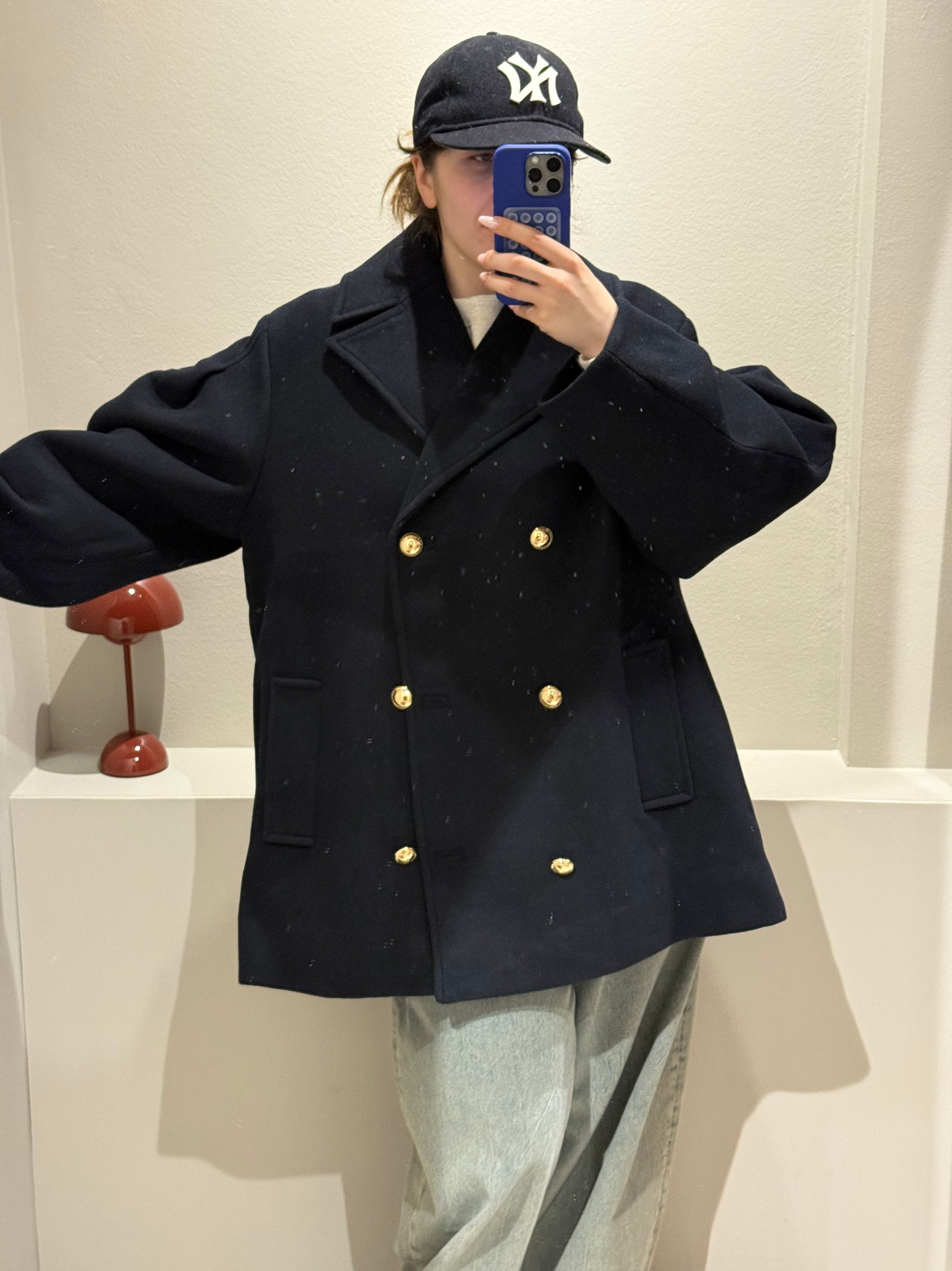 Frau macht Spiegelselfie, sie trägt eine dunkelblaue Cabanjacke und Jeans.