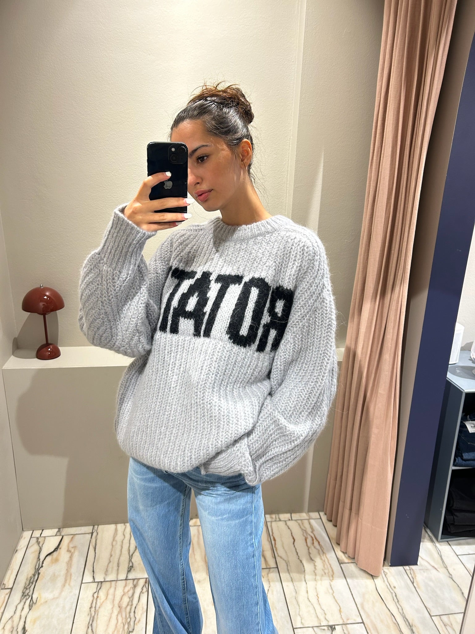 Frau macht Spiegelselfie, sie trägt Jeans und einen grauen kastigen Strickt mit Rotate Schriftzug.