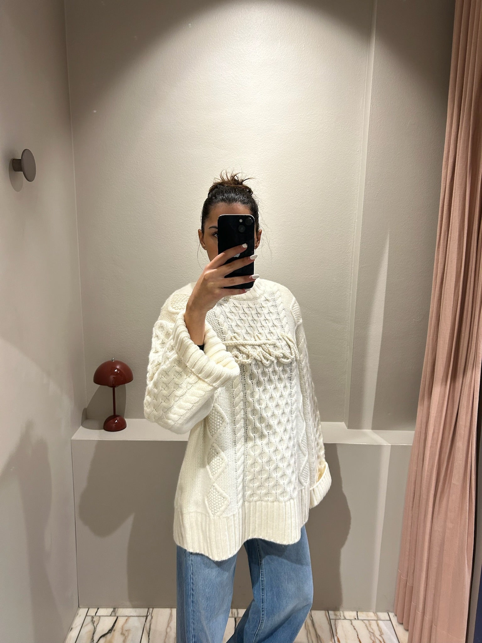 Frau macht Speigelselfie, sie trägt einen kastigem weißen Cable Knit Sweater und Jeans.