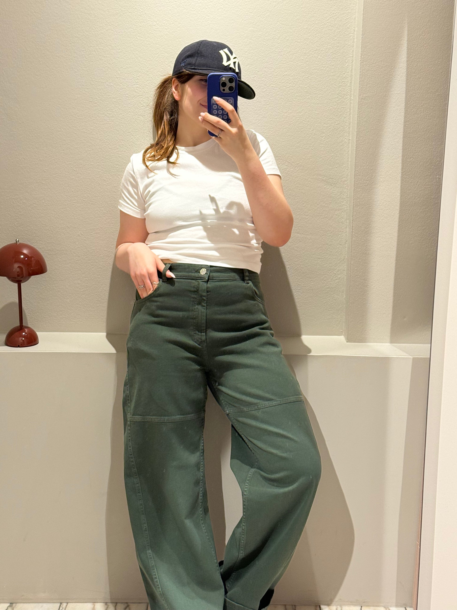 Frau macht Spiegelselfie, sie trägt eine grüne denim, weißes Tee und Kappe.