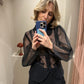 Frau macht Spiegelselfie, sie trägt schwarze Hose und schwarze transparente Bluse.